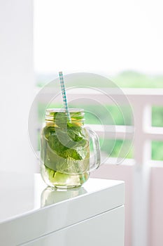 Tasty colorful drink with cold green tea, mint and lemon in a glass jar on a white kitchen background