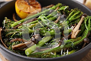 Tasty cooked broccolini, mushrooms and lemon in serving pan, closeup