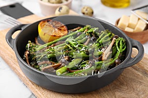 Tasty cooked broccolini, mushrooms and lemon on wooden board, closeup