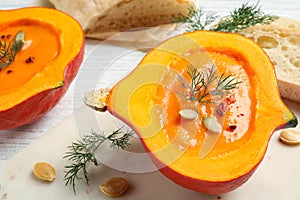 Tasty cream soup in pumpkin half on white wooden table