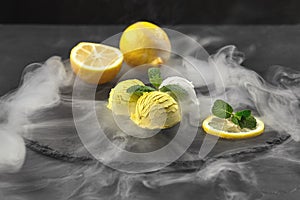 Tasty creamy and citrus lemon ice cream decorated with mint served on a stone slate over a black background.