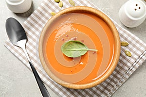 Tasty creamy pumpkin soup with basil in bowl on grey table, flat lay
