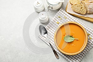 Tasty creamy pumpkin soup with basil in bowl on grey table, flat lay. Space for text