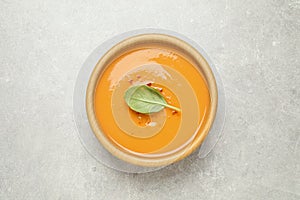 Tasty creamy pumpkin soup with basil in bowl on light grey table, top view