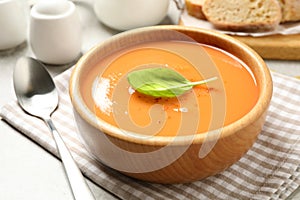 Tasty creamy pumpkin soup with basil in bowl on table