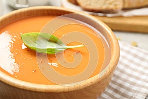 Tasty creamy pumpkin soup with basil in bowl on table, closeup