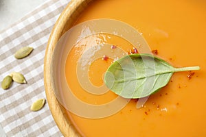 Tasty creamy pumpkin soup with basil in bowl on table, closeup