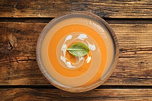 Tasty creamy pumpkin soup with basil in bowl on wooden table, top view