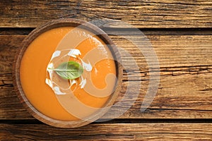 Tasty creamy pumpkin soup with basil in bowl on wooden table, top view. Space for text