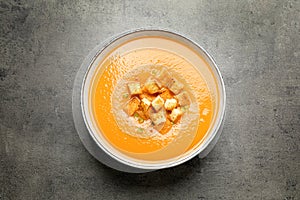 Tasty creamy pumpkin soup with croutons in bowl on grey table, top view