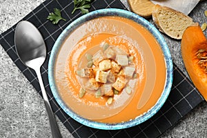 Tasty creamy pumpkin soup with croutons and seeds in bowl on grey table, flat lay