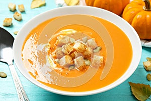 Tasty creamy pumpkin soup with croutons and seeds in bowl on light blue wooden table, closeup