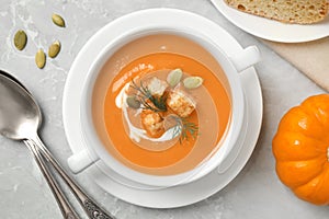 Tasty creamy pumpkin soup with croutons, seeds and dill in bowl on light grey table, flat lay