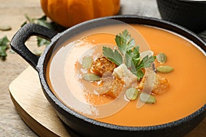 Tasty creamy pumpkin soup with croutons, seeds and parsley in bowl on table, closeup