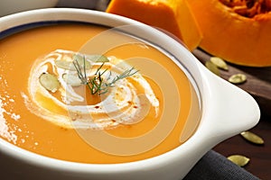 Tasty creamy pumpkin soup with dill and seeds in bowl on table, closeup