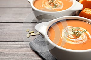Tasty creamy pumpkin soup with dill and seeds in bowl on wooden table. Space for text