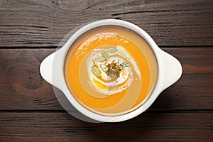 Tasty creamy pumpkin soup with dill and seeds in bowl on wooden table, top view