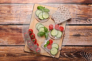 Tasty crispbreads, cucumber, tomatoes and basil on wooden table, flat lay