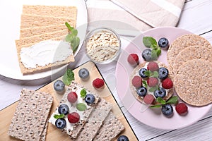 Tasty crispbreads, oatmeal, berries and mint on white wooden table, flat lay