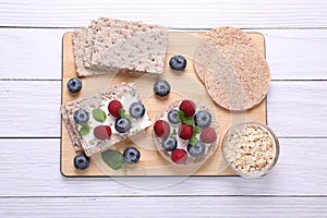 Tasty crispbreads, oatmeal, berries and mint on white wooden table, top view