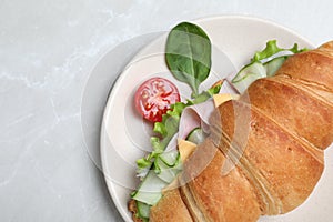 Tasty croissant sandwich with ham and cucumber on light grey marble table, top view