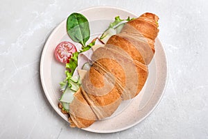 Tasty croissant sandwich with ham and cucumber on grey marble table, top view