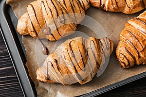 Tasty croissants with chocolate sauce on baking tray