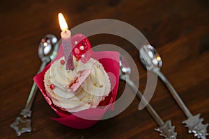 Tasty cupcake for birthday party with candel and spoons on a brown wooden table. Cakes decorated with white cheese cream