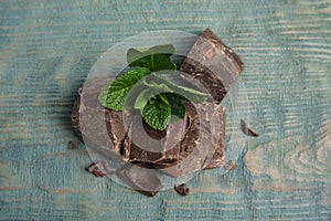 Tasty dark chocolate pieces with mint on blue wooden table, flat lay