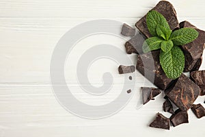 Tasty dark chocolate pieces with mint on white wooden table, flat lay. Space for text