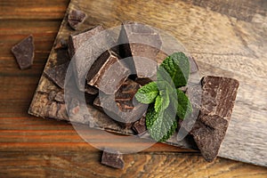 Tasty dark chocolate pieces with mint on wooden table, flat lay