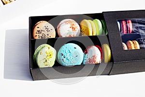 Tasty different colored macarons in black box on light background