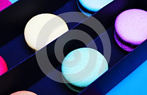 Tasty different colored macarons in black box on multicolored background