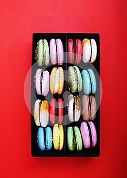 Tasty different colored macarons in black box on red background