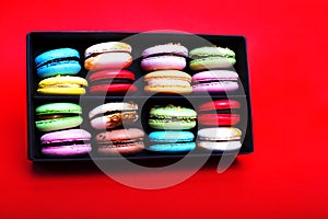 Tasty different colored macarons in black box on red background.