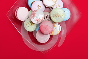 Tasty different colored macarons in dish on red backgroundn