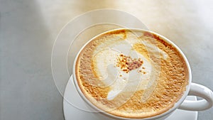 Tasty drinking, a cup of cappuccino coffee decorated with fluffy white and brown milk froth in white ceramic cup on gray table