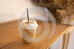 Tasty drinking, a cup of ice cappuccino coffee decorated with white milk froth in a tall plastic glass on brown wooden table