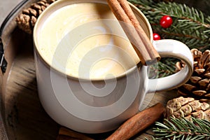 Tasty eggnog, cinnamon sticks and fir branches on wooden tray, closeup