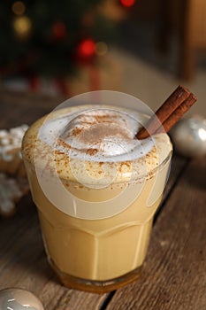 Tasty eggnog with cinnamon on wooden table against blurred festive lights, closeup