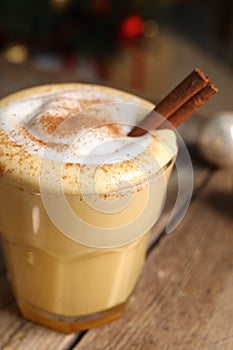 Tasty eggnog with cinnamon on wooden table against blurred festive lights, closeup