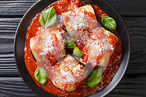 Tasty eggplant rolls stuffed with cheese and baked in tomato sauce close-up in a plate. Horizontal top view