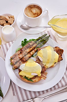 Tasty eggs Benedict, hollandaise sauce and aspargus covered with bacon