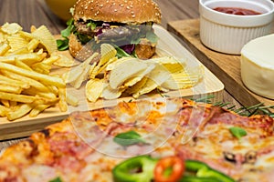 Tasty fast food on table. Pepperoni pizza and pizza Capricciosa , hamburger and potato chips