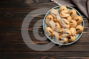 Tasty fortune cookies with predictions in plate on wooden table, top view. Space for text