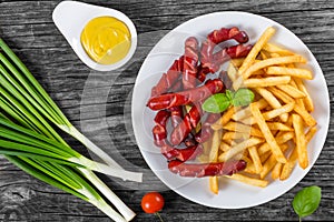 Tasty french fries and sausages on plate, top view