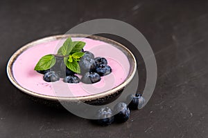 Tasty fresh blueberry yoghurt shake dessert in ceramic bowl standing on black dark table background