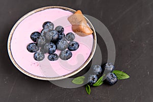 Tasty fresh blueberry yogurt shake dessert in ceramic bowl standing on black dark table background