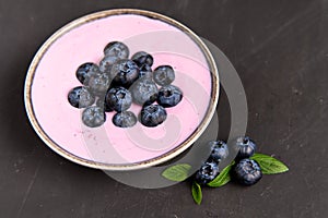 Tasty fresh blueberry yogurt shake dessert in ceramic bowl standing on black dark table background