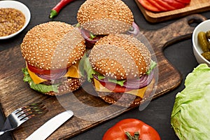 Tasty fresh cheeseburgers on wooden board with cutlery